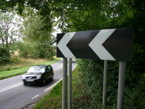 Black car on country road with a sharp bend warning sign