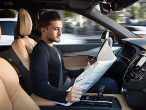 Driver reading newspaper at wheel of driverless Volvo