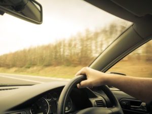 Image of man's arm holding steering wheel driving on road