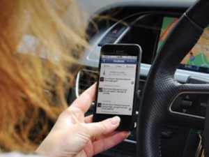 Woman holding mobile phone behind the wheel
