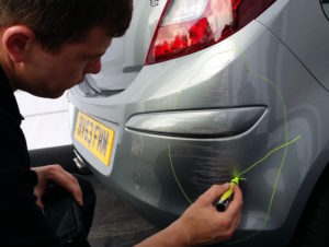 Man marking damaged car bumper for repair